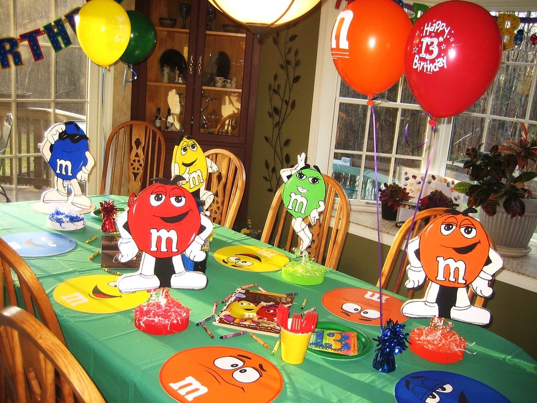 Ett fullt dekorerat kalasbord med M&M-karaktärer, färgglada ballonger och andra festartiklar.